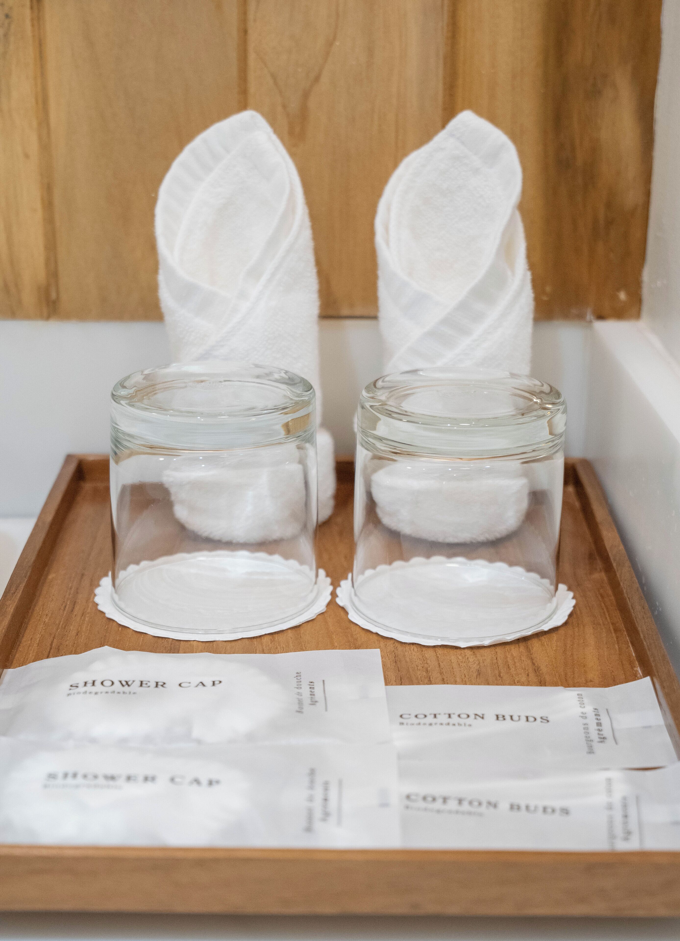 Dos frascos de vidrio transparentes con bastoncillos de algodón sobre una bandeja de madera, junto con paquetes de pañuelos etiquetados.