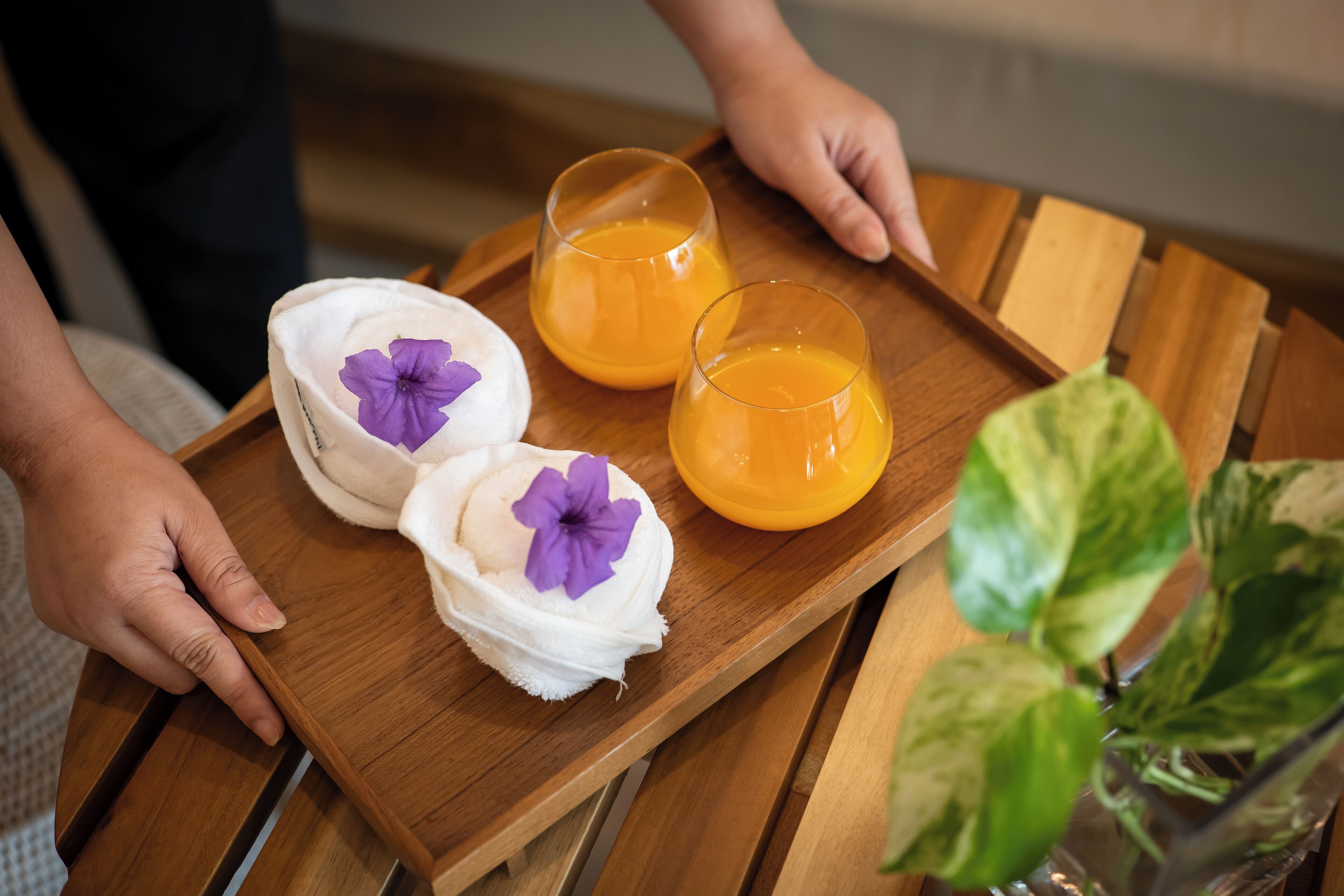 A wooden tray with two white containers and two glasses of orange juice, each with a purple flower.