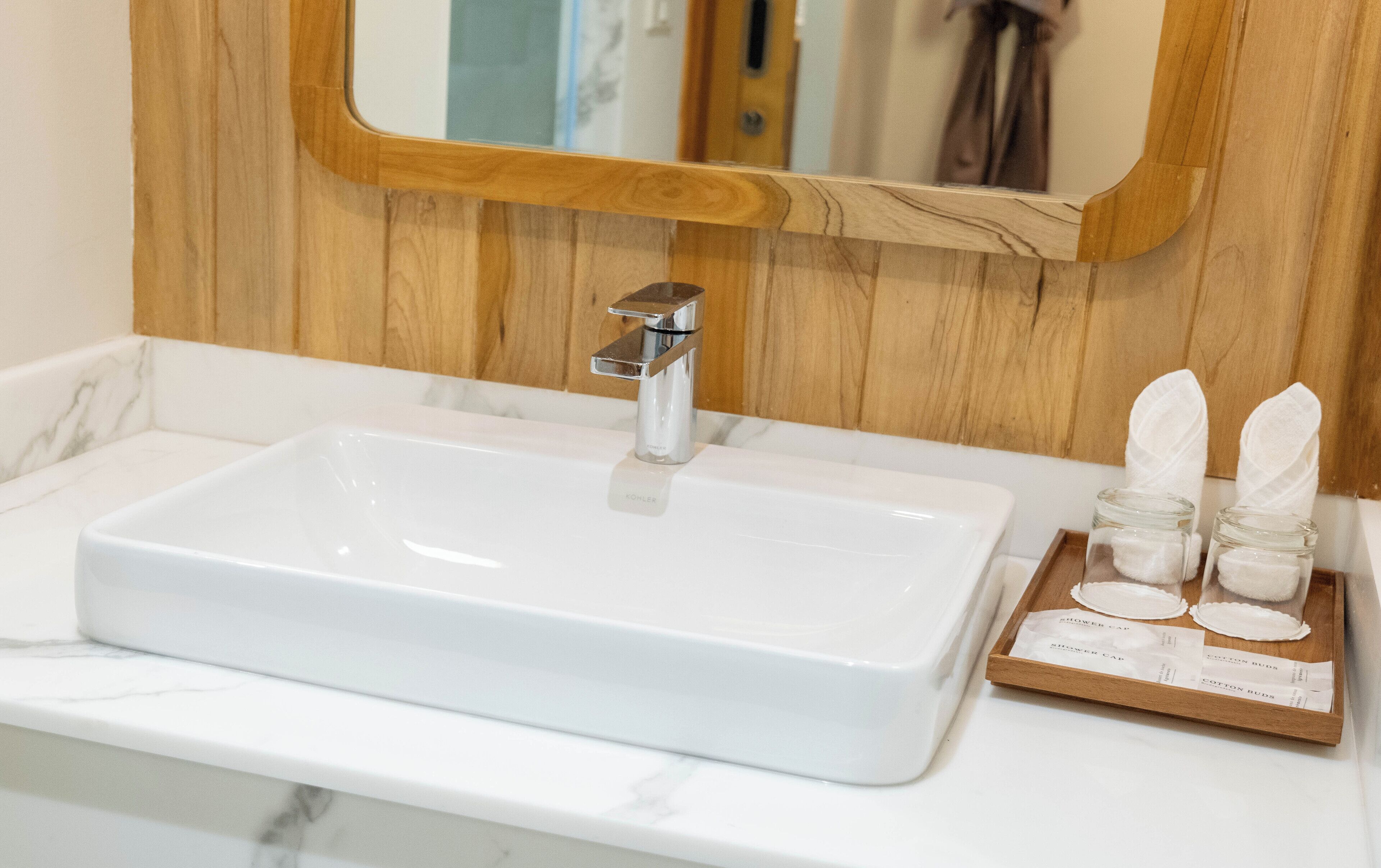 A bathroom with a white sink, chrome faucet, wooden wall paneling, and a mirror.