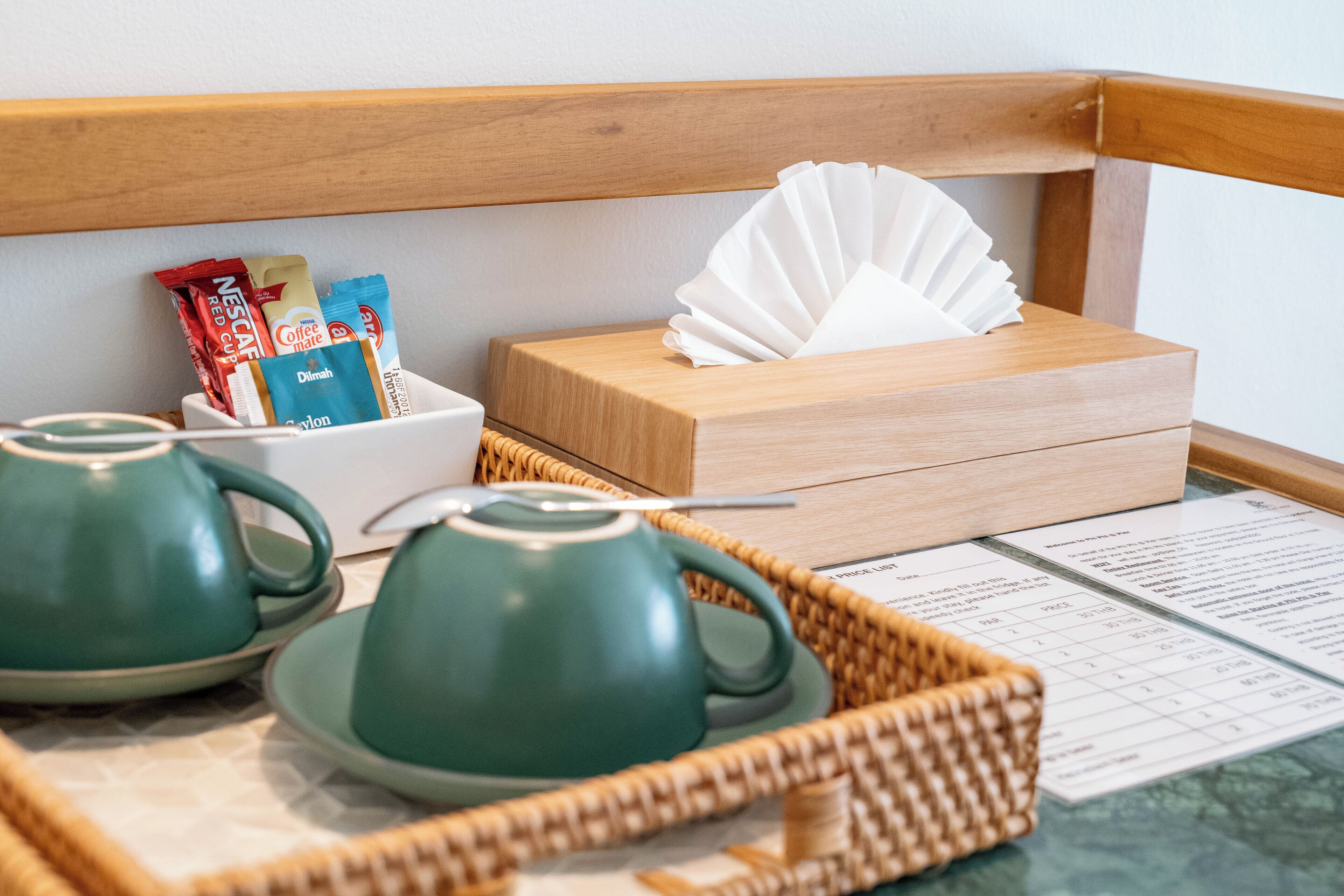 A breakfast setup with two green teapots, a basket of coffee packets, a tissue box, and a menu on a table.