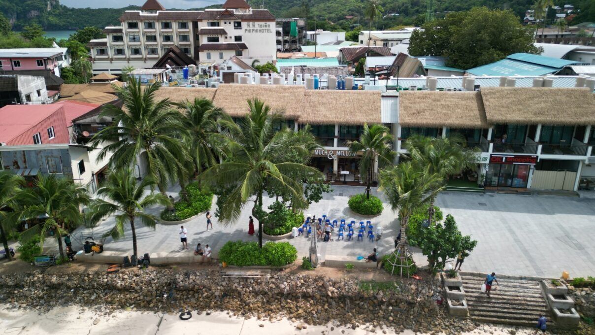 A hotel with a thatched-roof structure, palm trees, and a paved area with seating.