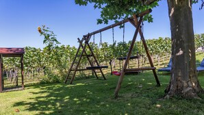 A playground with swings and a tree, surrounded by a grassy area and a vineyard in the background. - Room '102' with Shared Garden, Balcony and Wi-Fi (Hagnau)