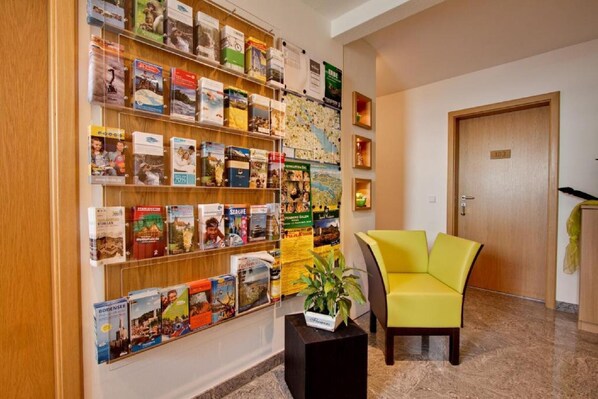 Un vestíbulo de hotel con una estantería llena de libros de viajes, un sillón amarillo y una puerta con el rótulo '103'.