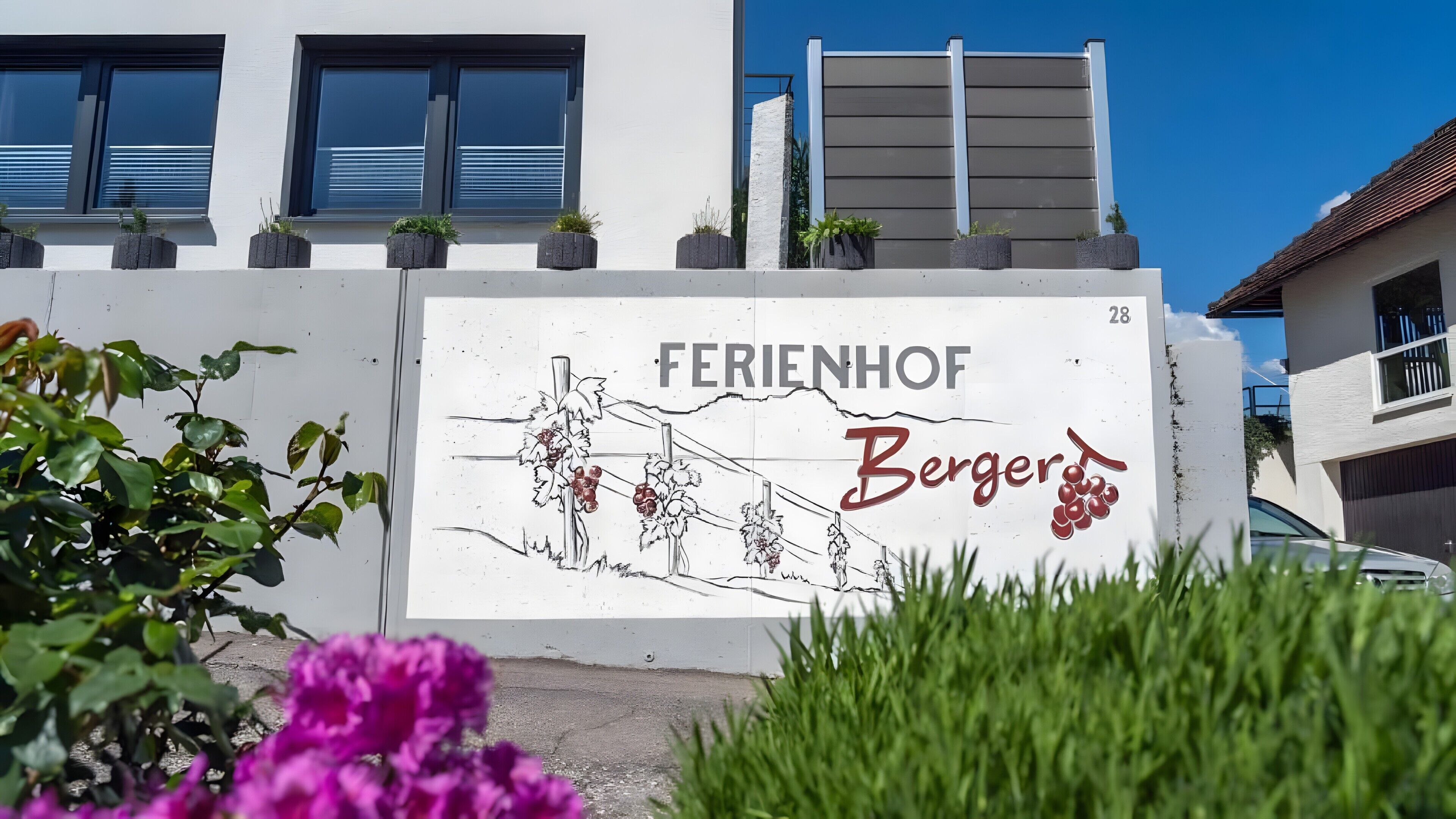 Ein Gebäude mit einem Schild, auf dem 'FERIENHOF Berger' steht, und einer Zeichnung von Weinreben.