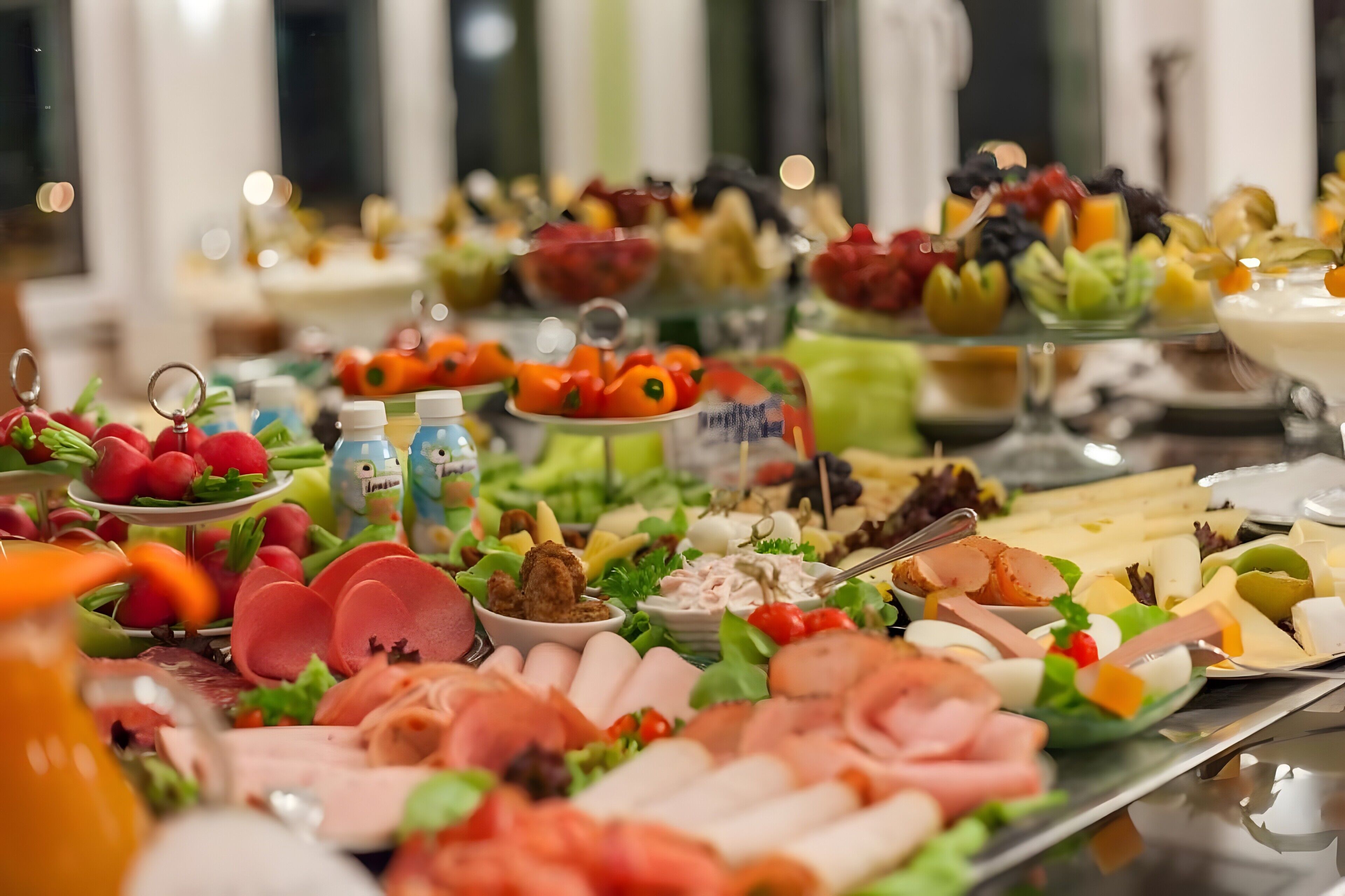 A buffet with various food items including meats, cheeses, fruits, and salads.