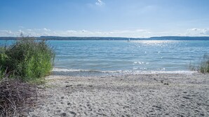 A beach with clear water, a distant sailboat, and a hilly landscape. - Room '206' with Shared Garden, Balcony and Wi-Fi (Hagnau)