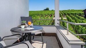 A balcony with a table, chairs, a potted plant, a glass of orange juice, and a view of a vineyard. - Room '103' with Shared Garden, Balcony and Wi-Fi (Hagnau)