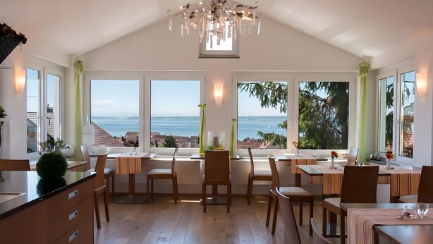 A spacious dining area with large windows, a chandelier, and a view of the ocean. - Room '103' with Shared Garden, Balcony and Wi-Fi (Hagnau)
