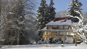 A two-story house with a snow-covered roof, surrounded by snow-laden trees. - Apartment 1 with Alpine Views, Outdoor Seating, and Wi-Fi (Schopfheim)
