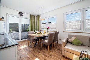 A modern kitchen with a dining area, a sofa, and a large window with blinds. - Apartment '301' with Shared Garden, Wi-Fi and Air Conditioning (Hagnau)