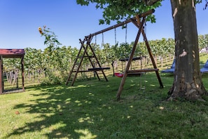 A playground with swings and a tree, surrounded by a grassy area and a vineyard in the background. - Apartment '301' with Shared Garden, Wi-Fi and Air Conditioning (Hagnau)