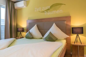 A hotel room with a bed, two bedside lamps, a wall-mounted air conditioner, and a wall with text. - Apartment '301' with Shared Garden, Wi-Fi and Air Conditioning (Hagnau)