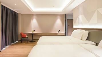 A hotel room with two beds, a small table with a chair, a large window with curtains, and a geometric wall design.