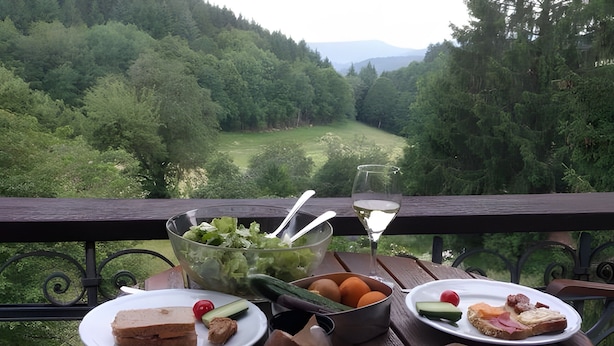 Una mesa con comida y una copa de vino, con vistas a un valle boscoso.