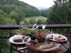 Ein Tisch mit Speisen und einem Weinglas, mit Blick auf ein bewaldetes Tal.