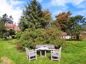 Ein Garten mit Holztisch und -stühlen, umgeben von üppiger Bepflanzung und Bäumen.