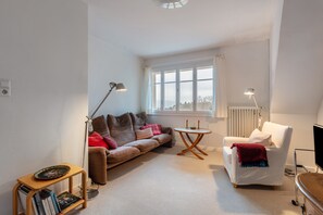 A living room with a sofa, a small round table, a white armchair, a bookshelf, and a large window. - Vacation apartment '2' with mountain view, private balcony and Wi-Fi (Schopfheim)