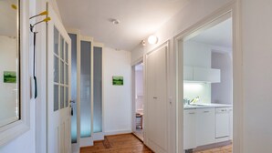 Un pasillo con piso de madera que conduce a una cocina con armarios blancos y un lavamanos.