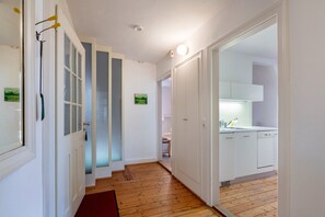 Un pasillo con piso de madera que conduce a una cocina con armarios blancos y un lavamanos.