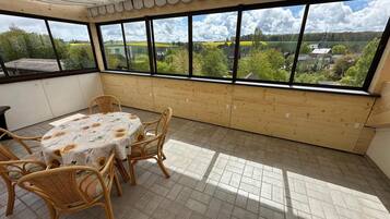 A covered patio with a table and chairs, large windows, and a view of a green landscape.