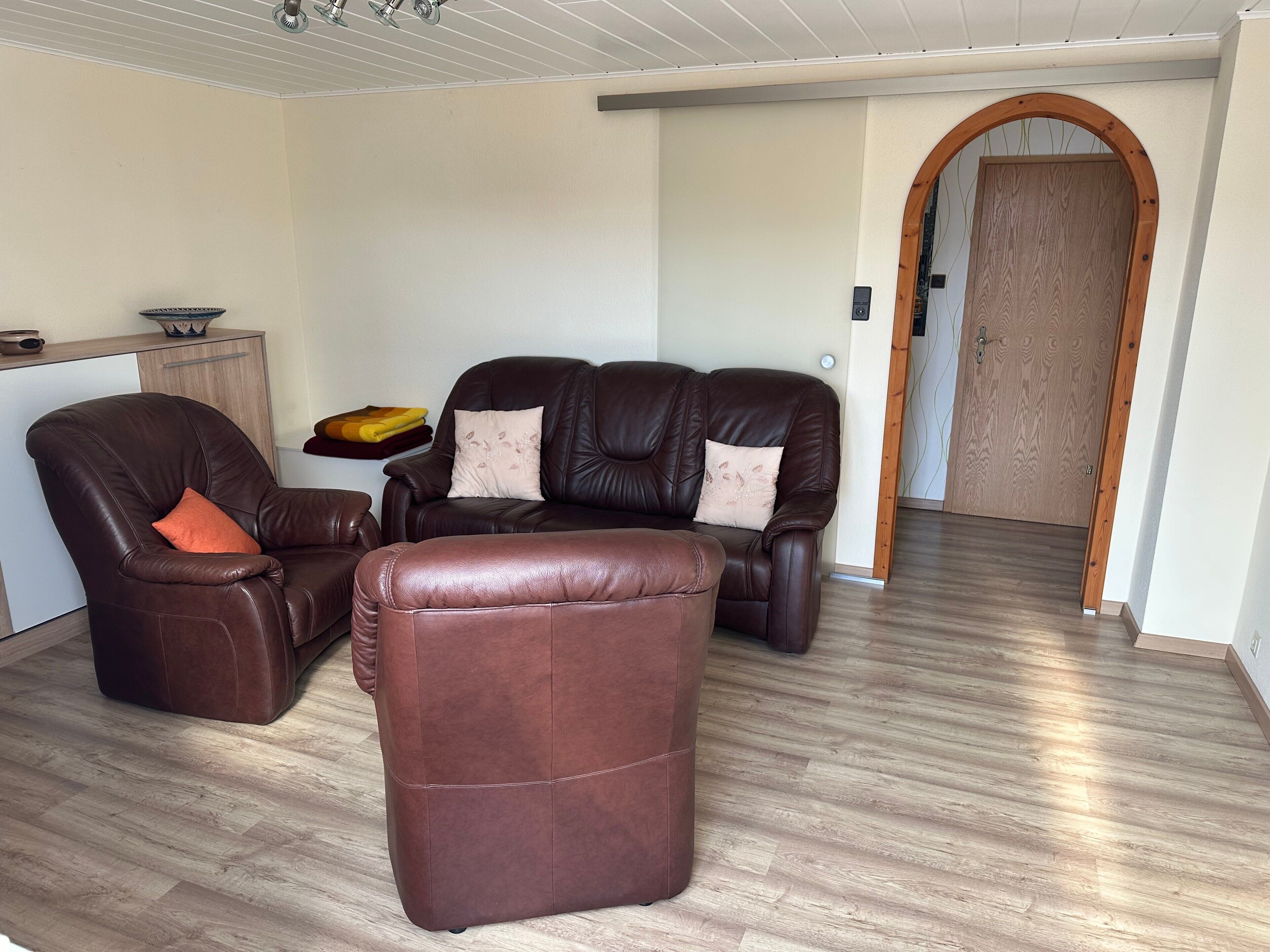 Un salon avec un canapé en cuir marron, un pouf assorti et un meuble en bois.