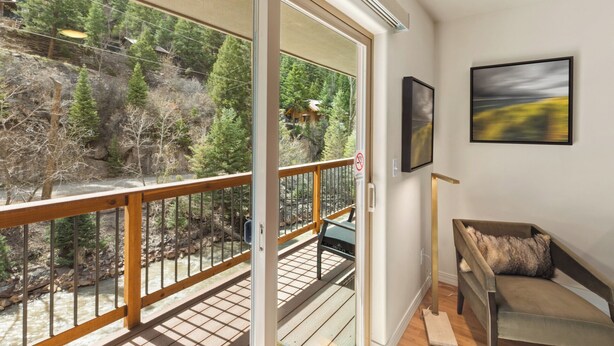 A balcony with a view of a forest and a river, a sofa, and two framed pictures on the wall.