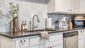 A modern kitchen with patterned backsplash, stainless steel appliances, and white cabinetry. - The Westside Collective (Westworth Village)