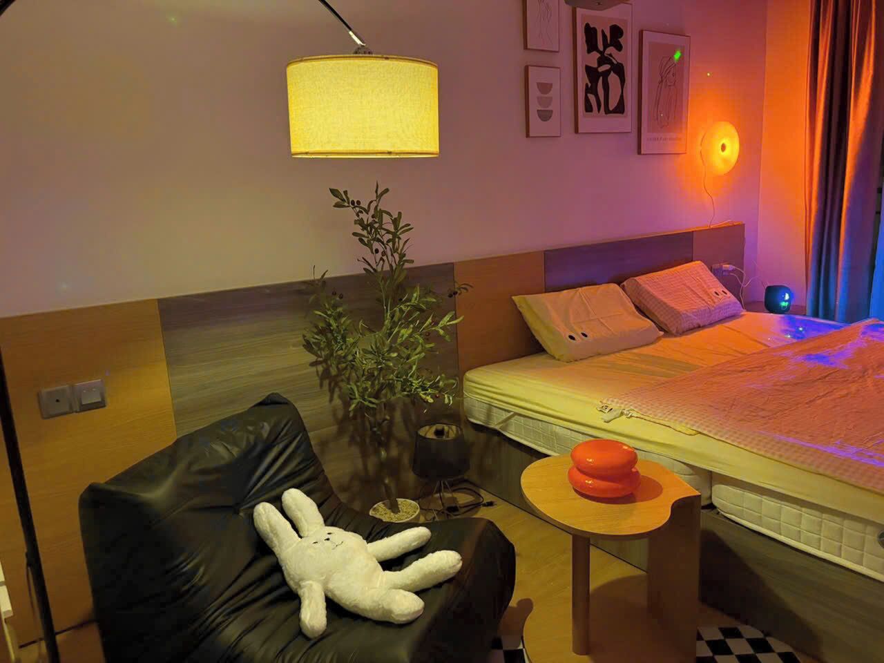 Ein Hotelzimmer mit einem Bett, einem kleinen Tisch mit Lampe, einem Sessel mit Stofftier und einer Topfpflanze.