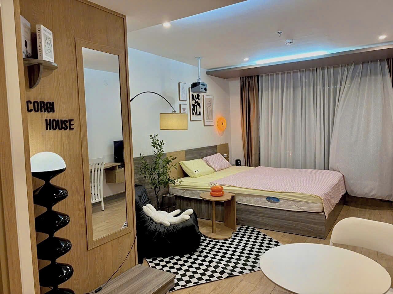 Quarto de hotel pequeno com uma cama, uma escrivaninha, uma cadeira, uma mesinha e um espelho.