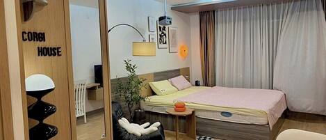 Quarto de hotel pequeno com uma cama, uma escrivaninha, uma cadeira, uma mesinha e um espelho.