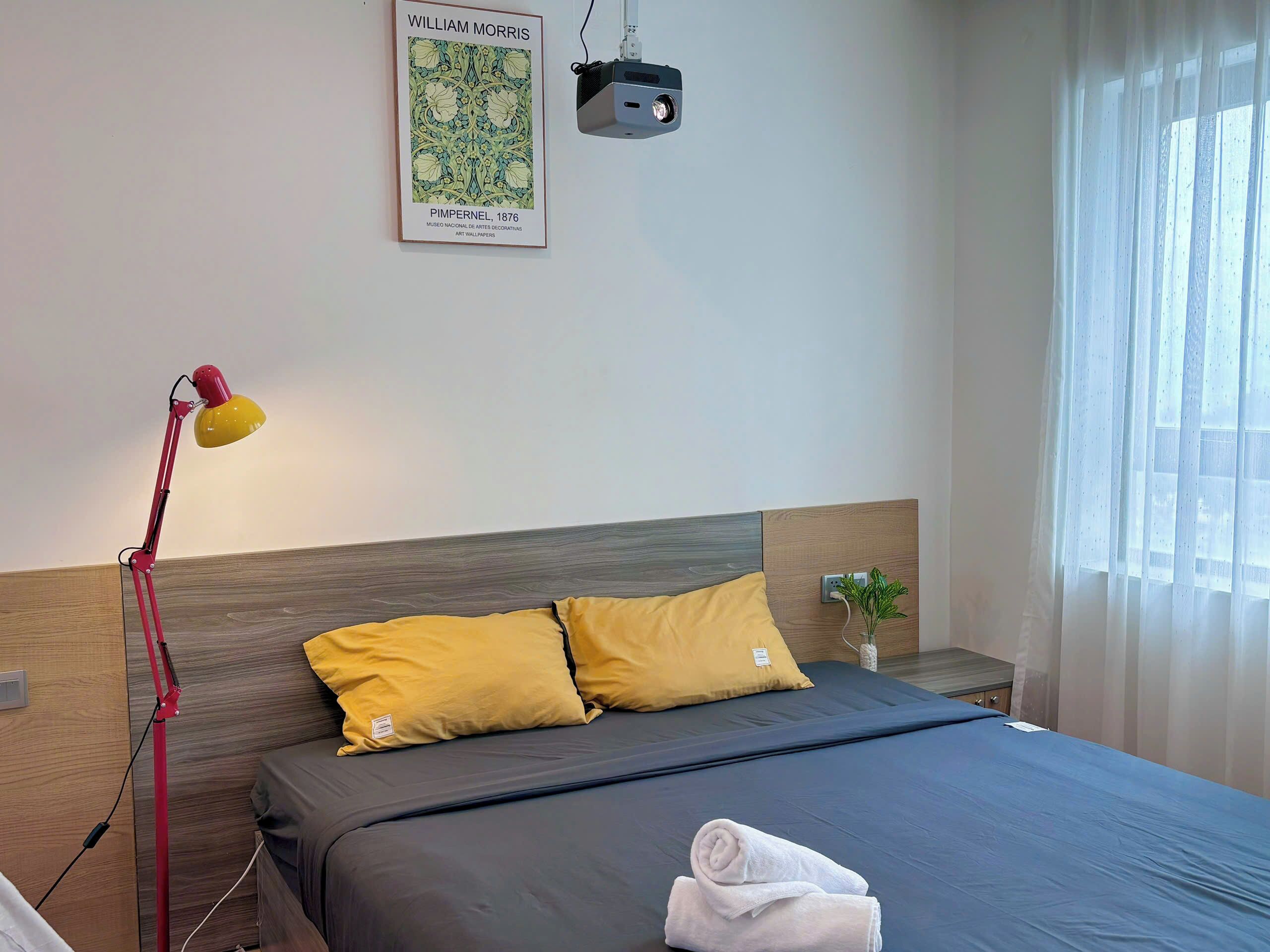A neatly made bed with two yellow pillows, a bedside lamp, and a framed artwork on the wall.