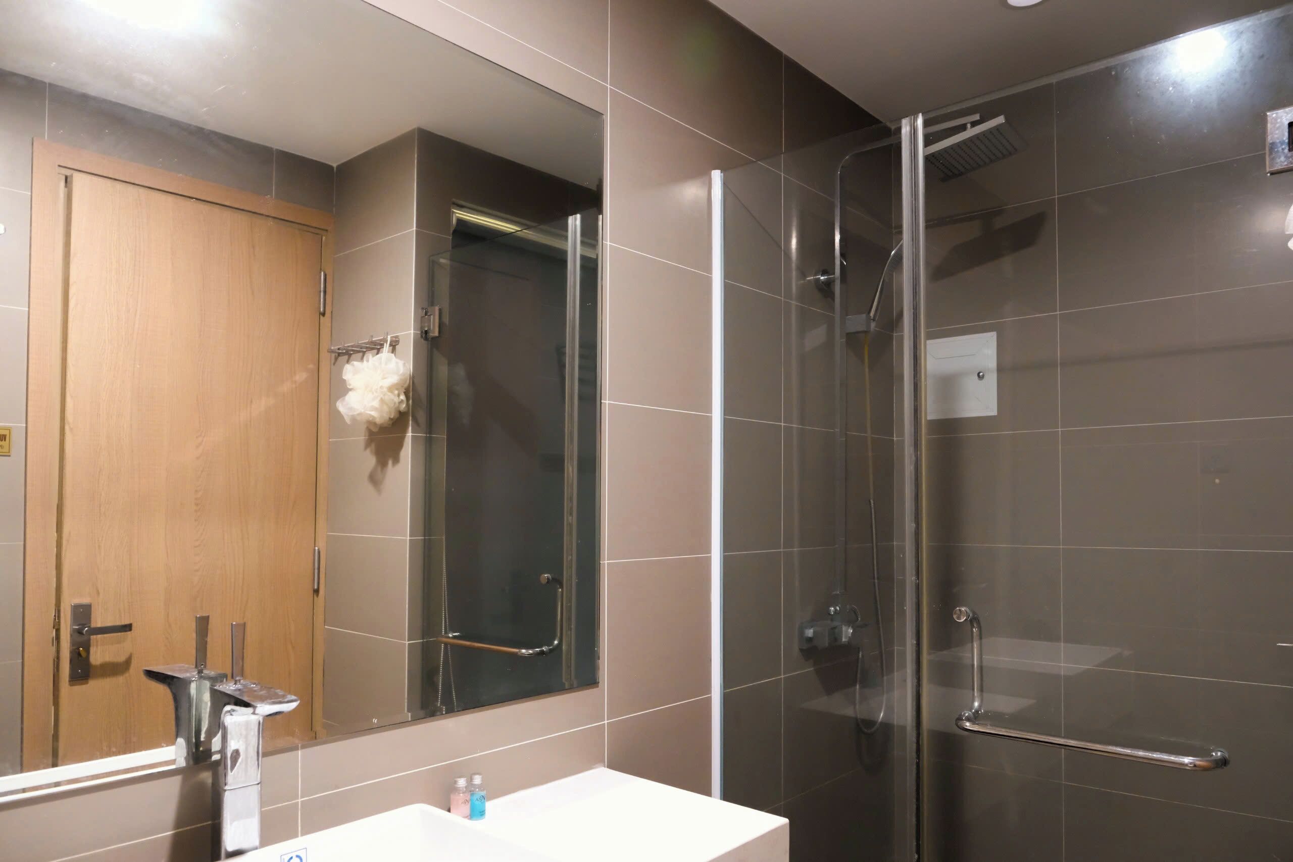 A bathroom with a glass shower enclosure, a wooden door, and a white sink.