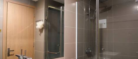 A bathroom with a glass shower enclosure, a wooden door, and a white sink.