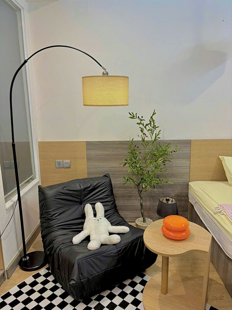 Une pièce moderne avec un fauteuil en cuir noir, une petite table en bois sur laquelle se trouve un bol orange, un lampadaire et une plante en pot.