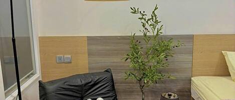Une pièce moderne avec un fauteuil en cuir noir, une petite table en bois sur laquelle se trouve un bol orange, un lampadaire et une plante en pot.