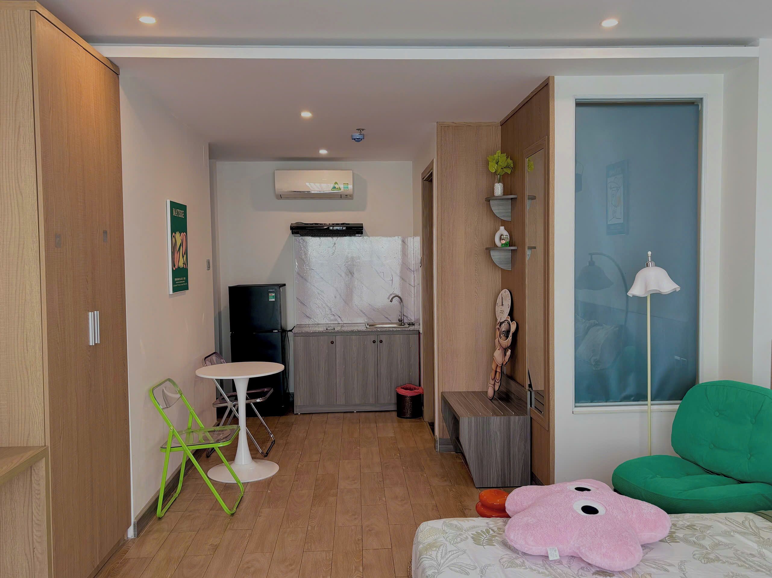 Un espace de vie compact comprenant un coin cuisine, une petite table à manger, une chaise verte, un jouet en peluche rose et un canapé vert.