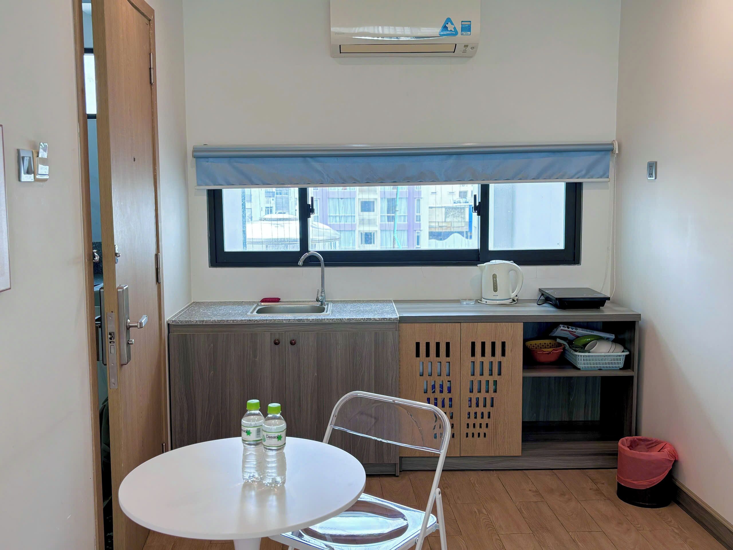 A compact kitchen with a window, a sink, a kettle, and a table with two water bottles.