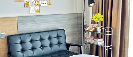 A modern living room with a black sofa, a small round yellow table, and a metal shelf with books and flowers.
