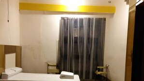 A hotel room with two beds, a small table, a chair, a window with curtains, and a colorful rug. - Giggler (Jamnagar)