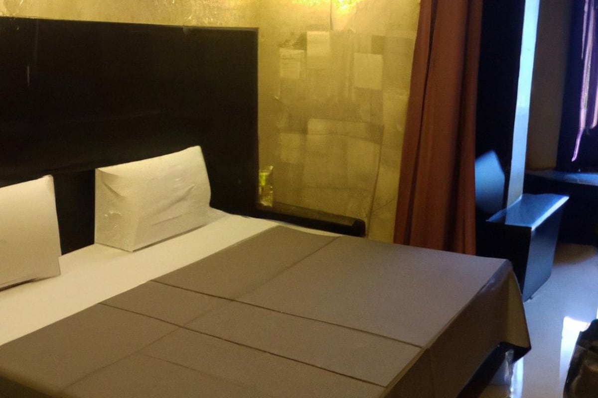 A hotel room with a large bed, a headboard, a nightstand, and a wall-mounted light fixture.