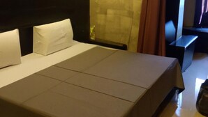 A hotel room with a large bed, a headboard, a nightstand, and a wall-mounted light fixture. - Giggler (Jamnagar)