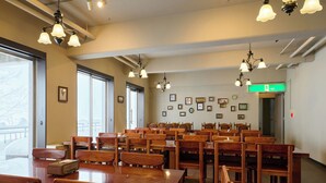 A spacious dining area with wooden tables and chairs, ceiling lights, and framed pictures on the walls. - HOTEL ST.MORITZ (Yuzawa)