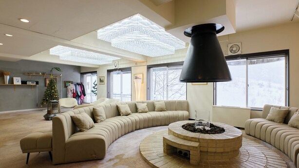 A spacious living room with a large L-shaped beige sofa, a round coffee table, and a modern chandelier. - HOTEL ST.MORITZ (Yuzawa)