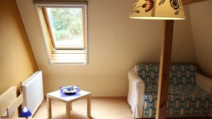 A room with a bunk bed, a small table with a lamp, a window with blinds, and a patterned sofa.