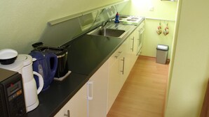 A compact kitchen with a sink, a coffee maker, a kettle, and a trash bin.