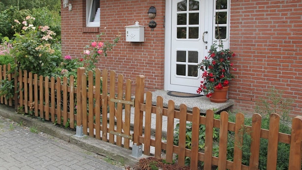 A brick house with a white door, a small window, and a wooden fence.