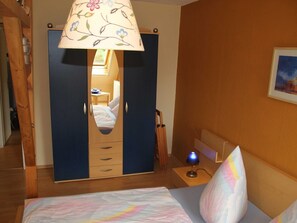 Un dormitorio con cama, mesita de noche, lámpara, armario y espejo.