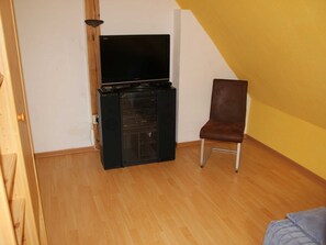 Una habitación con una televisión de pantalla plana, una silla marrón y suelo de madera.