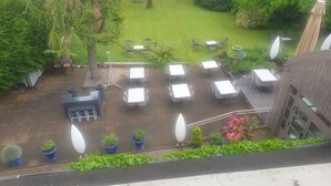 A patio area with multiple tables and chairs, surrounded by greenery and a wooden deck.