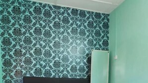 A bed with a patterned bedspread and pillows, a dark headboard, and a wall with a floral wallpaper pattern. - Tambun D'Mewah homestay (Ipoh)